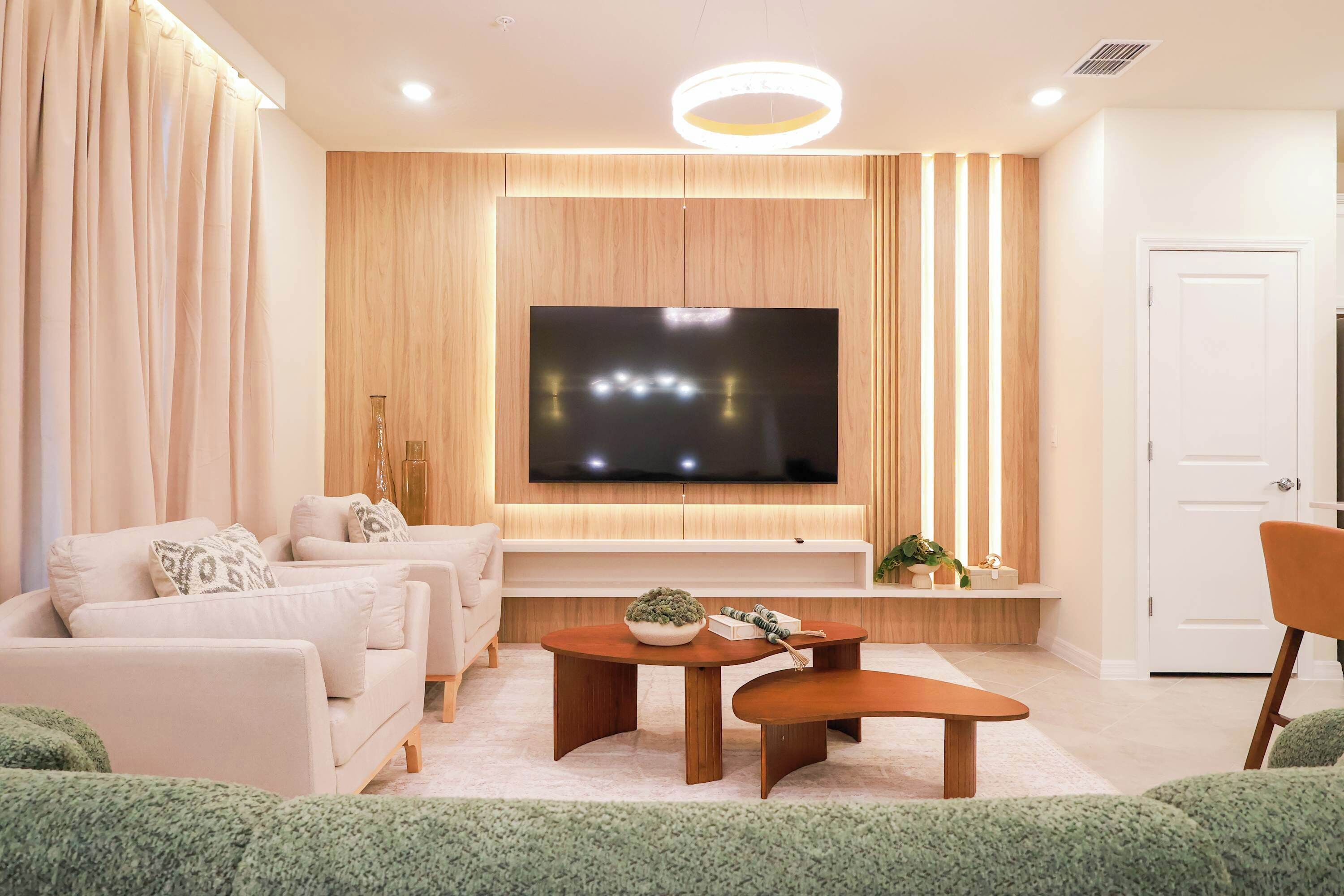 A modern living room with a flat-screen TV, sofas, a coffee table, and a door.