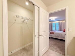Een slaapkamer met een bed, een raam met gordijnen en een deur naar een gang.