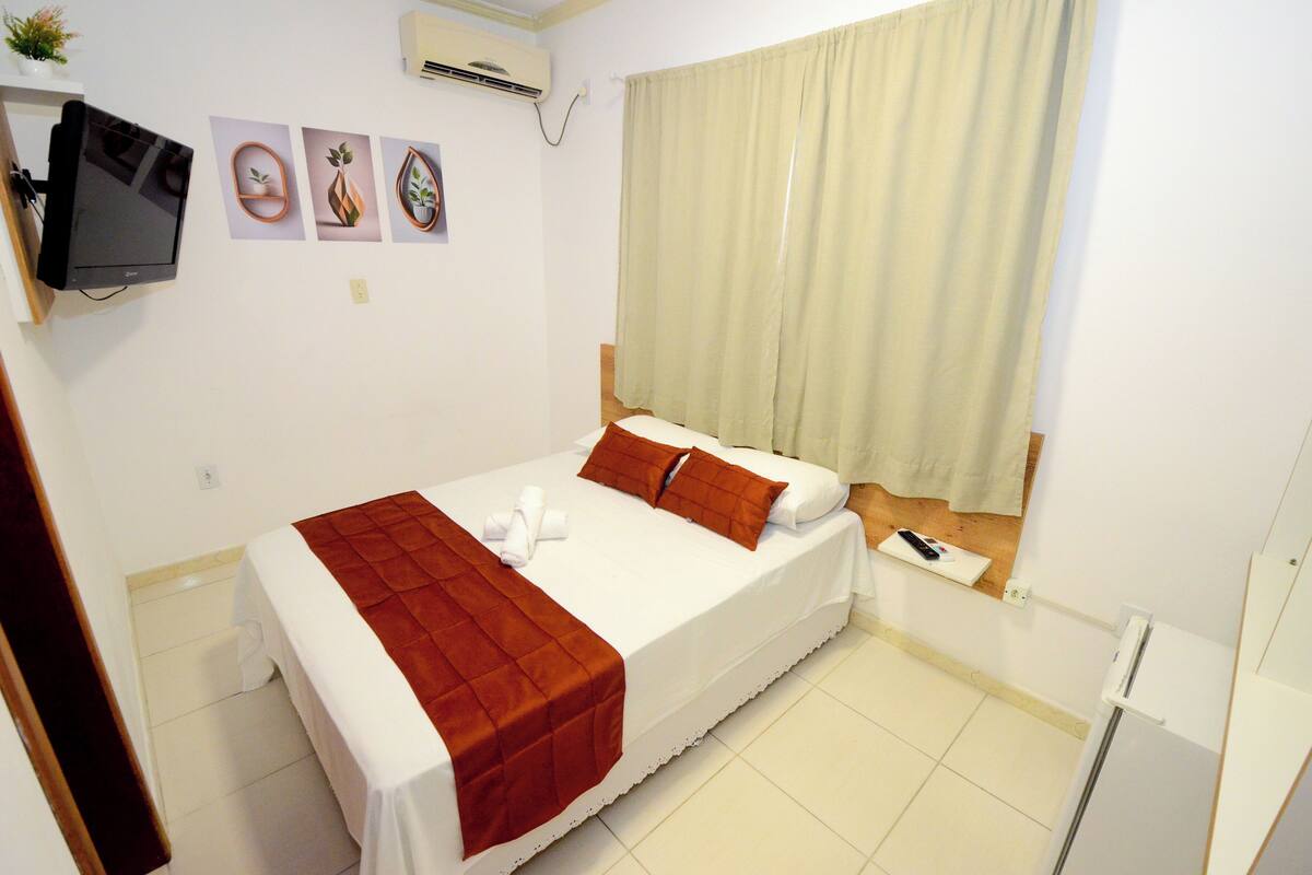 A single bed with a red blanket, white pillows, and a remote control on the nightstand.