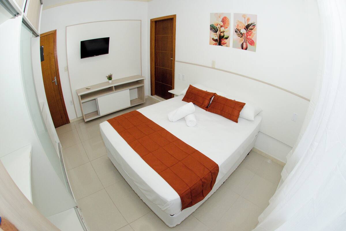 A bedroom with a bed, a TV mounted on the wall, a wooden door, and a painting.