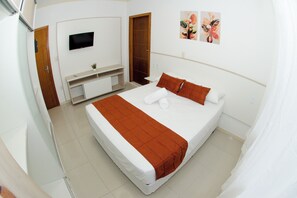 Un dormitorio con una cama, un televisor montado en la pared, una puerta de madera y un cuadro.