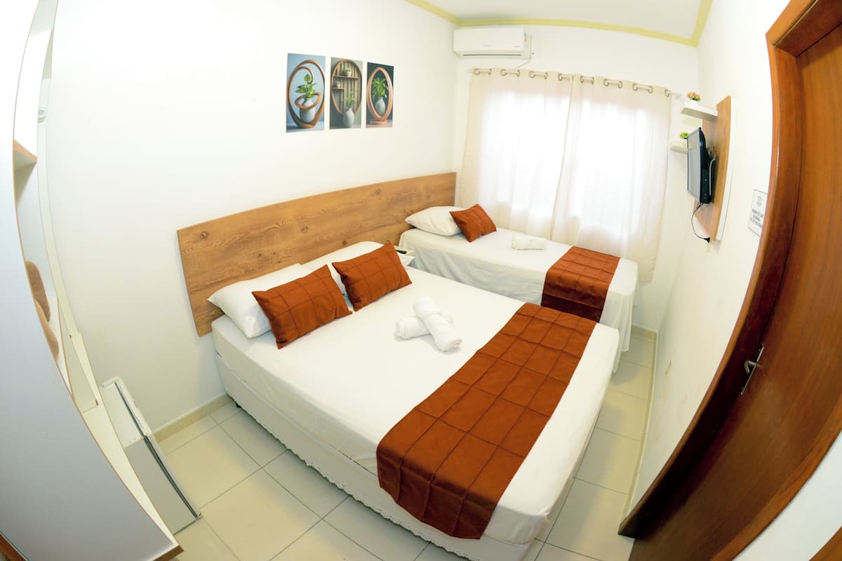 A hotel room with two beds, a wooden headboard, a TV, and a window with curtains.