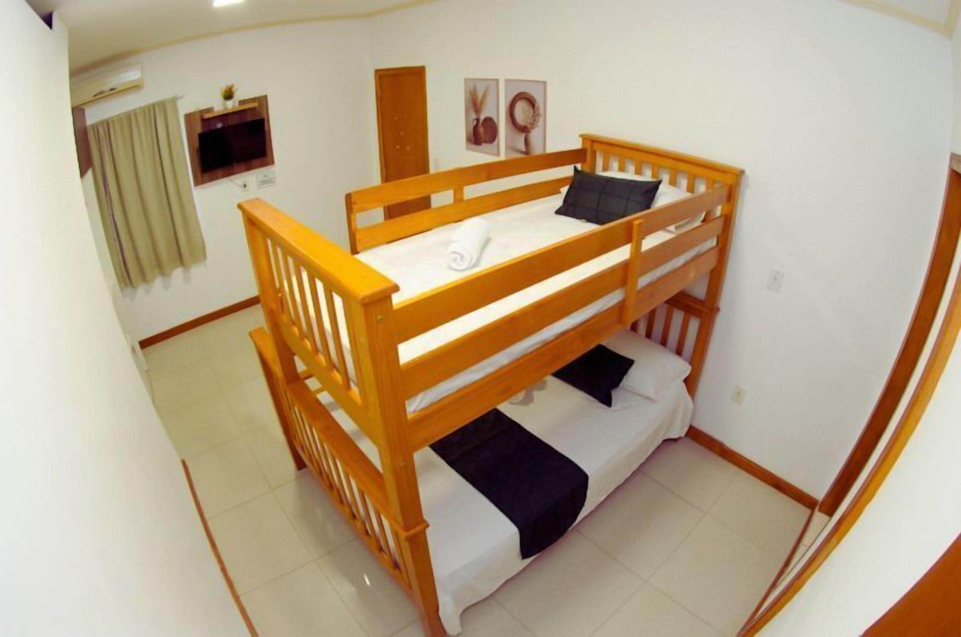 Habitación con literas de madera, una ventana pequeña y un televisor instalado en la pared.