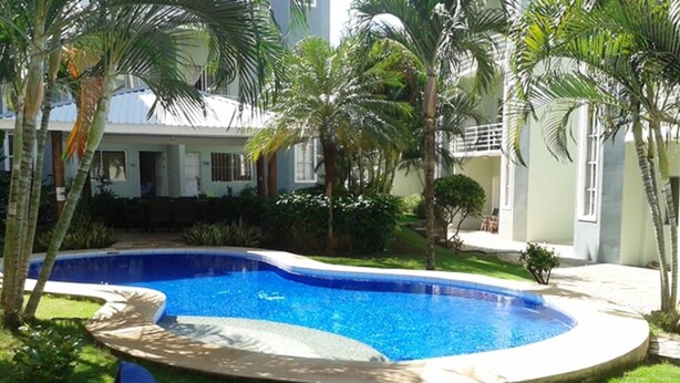 A swimming pool with a lounge chair and palm trees. - Cozy 2-bedroom apartment in charming Tamarindo with AC (Tamarindo)