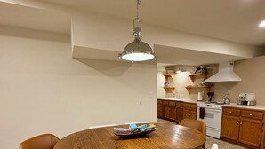 Een eetgedeelte met een ronde houten tafel, vier stoelen en een hanglamp.