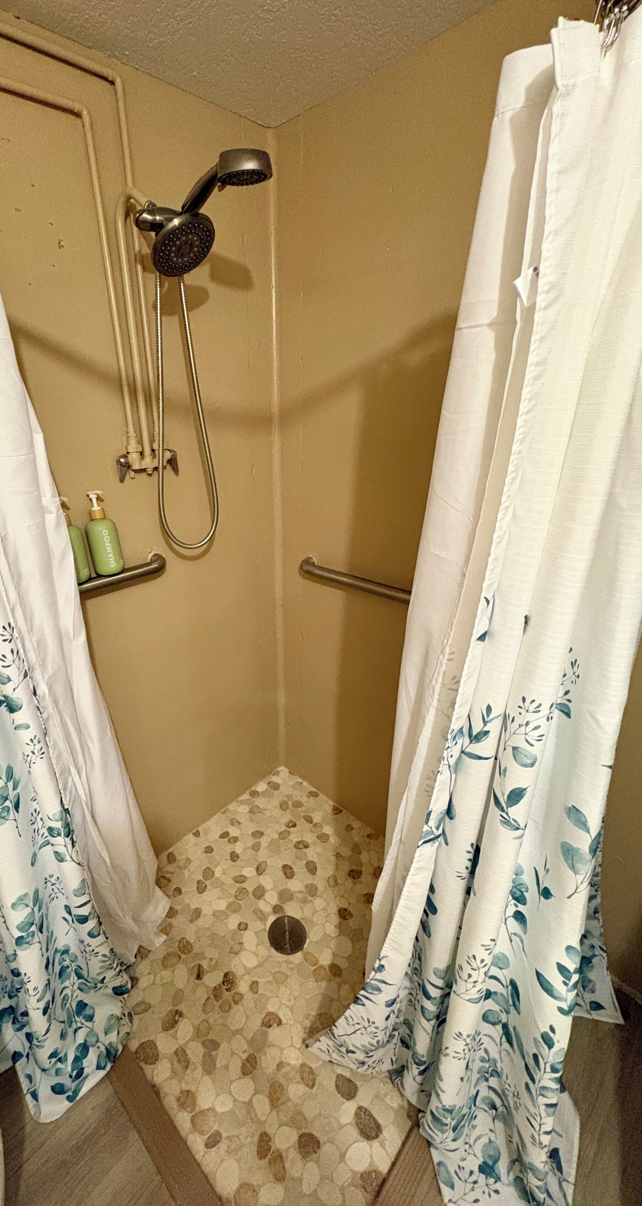 Un espace douche équipé d’un pommeau de douche mobile, d’une barre d’appui et d’un rideau de douche.