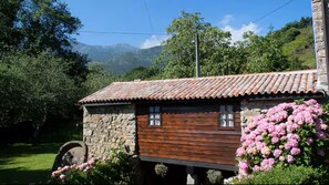 A rustic stone building with a wooden extension, a wheel, and pink flowers. - Sotu Mill (Colunga)