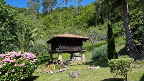 Une construction traditionnelle en bois, dotée d’un toit en tuiles, entourée d’une végétation luxuriante et de plantes en fleurs.