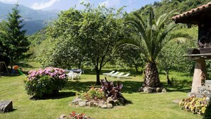 Un jardín con una palmera, una construcción de piedra y un parque infantil.