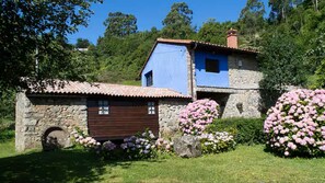 A stone building with a wooden door and a blue upper section. - Sotu Mill (Colunga)