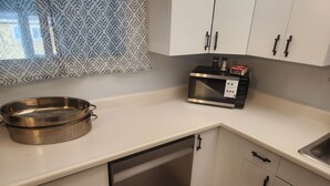 Una cocina con armarios blancos, lavavajillas de acero inoxidable, microondas y persiana con diseño.