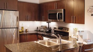 A modern kitchen with stainless steel appliances, a granite countertop, and wooden cabinets. - Upscale Toronto Condo | Monthly Stay (Toronto)