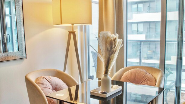A modern hotel room with a glass table, two chairs, a floor lamp, and a vase with dried plants. - Upscale Toronto Condo | Monthly Stay (Toronto)