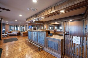 A reception area with a wooden reception desk, leather seating, and a stone accent wall. - Pinedale Hotel & Suites (Pinedale)