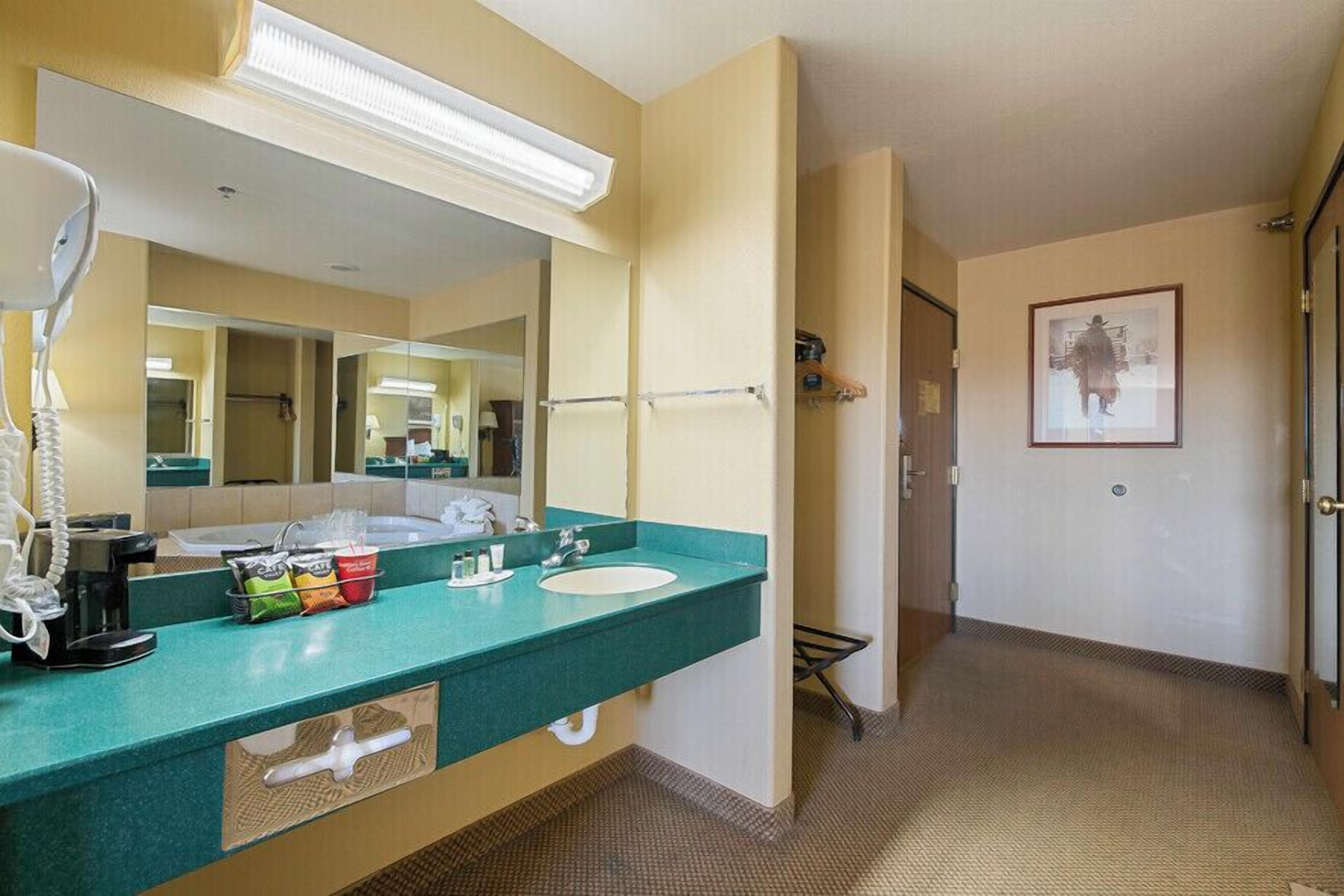 Een hotelbadkamer met een groen aanrecht, een wastafel, een spiegel, een telefoon en toiletartikelen.