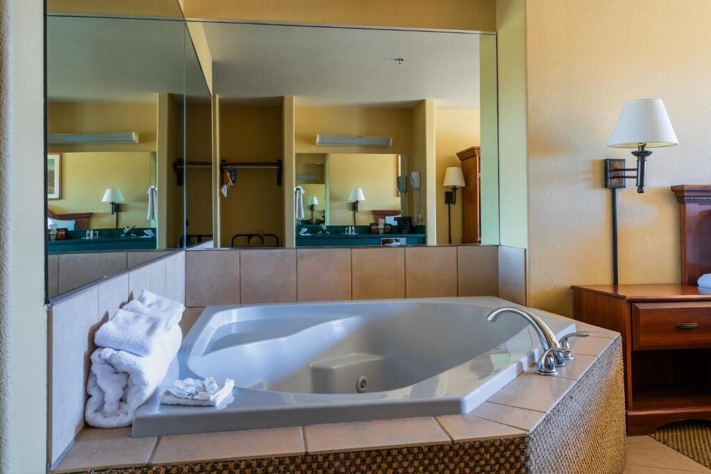 Un baño de hotel con una bañera grande, un espejo y una tocador con una lámpara.