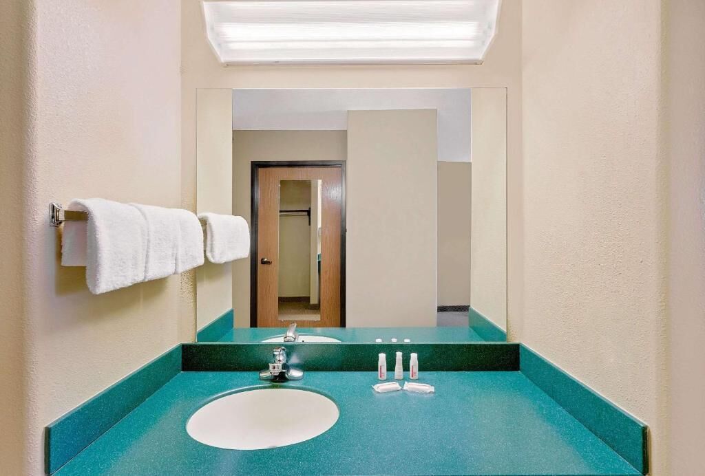 A bathroom with a teal countertop, a white sink, and a mirror. There are white towels hanging on a rack and a door leading to another room.
