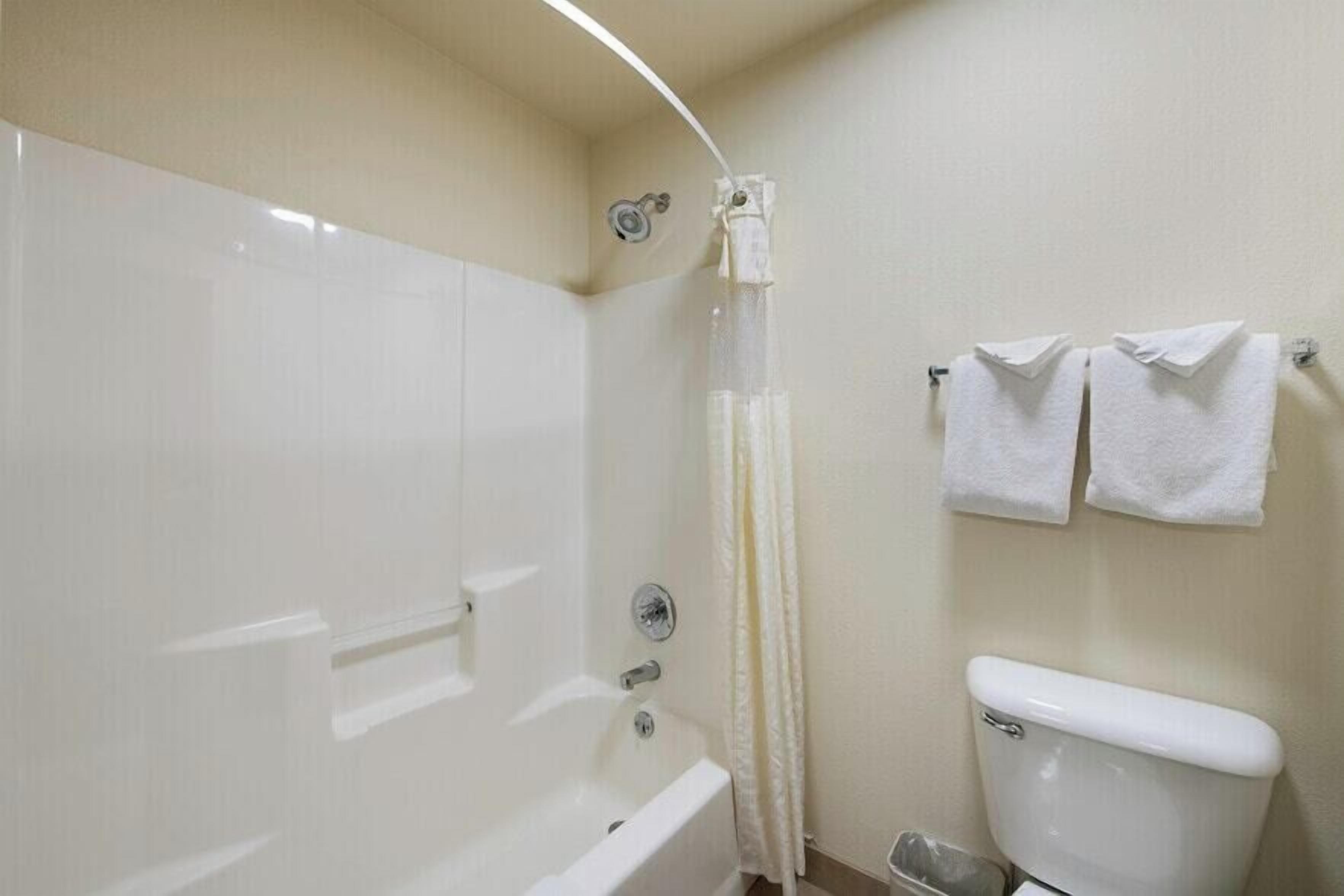 Un baño con bañera, cortina de ducha, inodoro y dos toallas en un perchero.