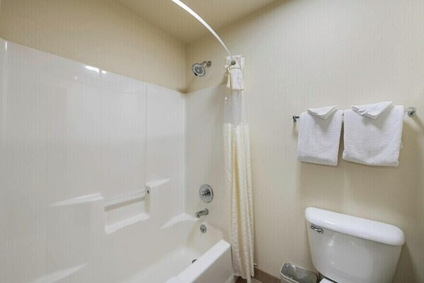 Un baño con bañera, cortina de ducha, inodoro y dos toallas en un perchero.