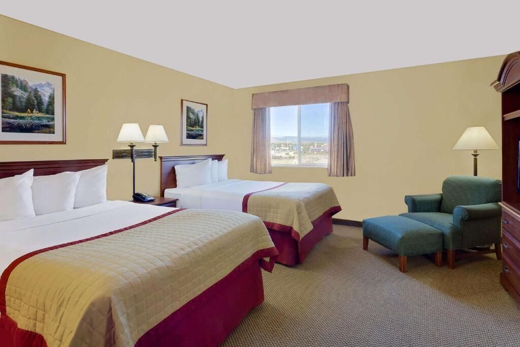 Habitación de hotel con dos camas, una silla, un escritorio, lámparas y una ventana con vistas.