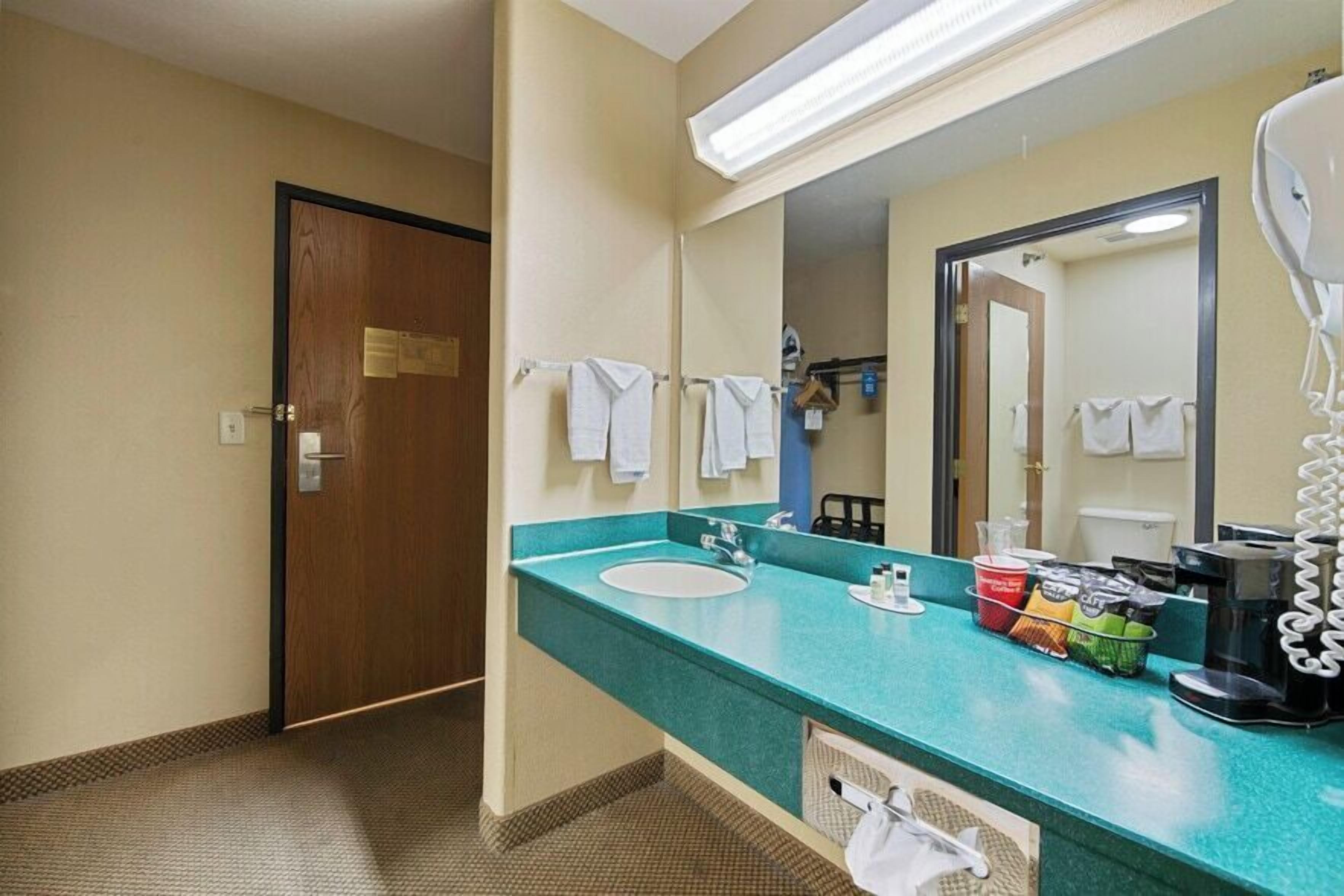A hotel bathroom with a sink, mirror, towel rack, and a coffee maker.