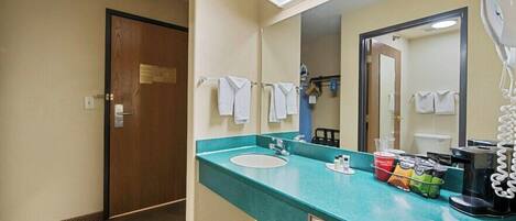 A hotel bathroom with a sink, mirror, towel rack, and a coffee maker.