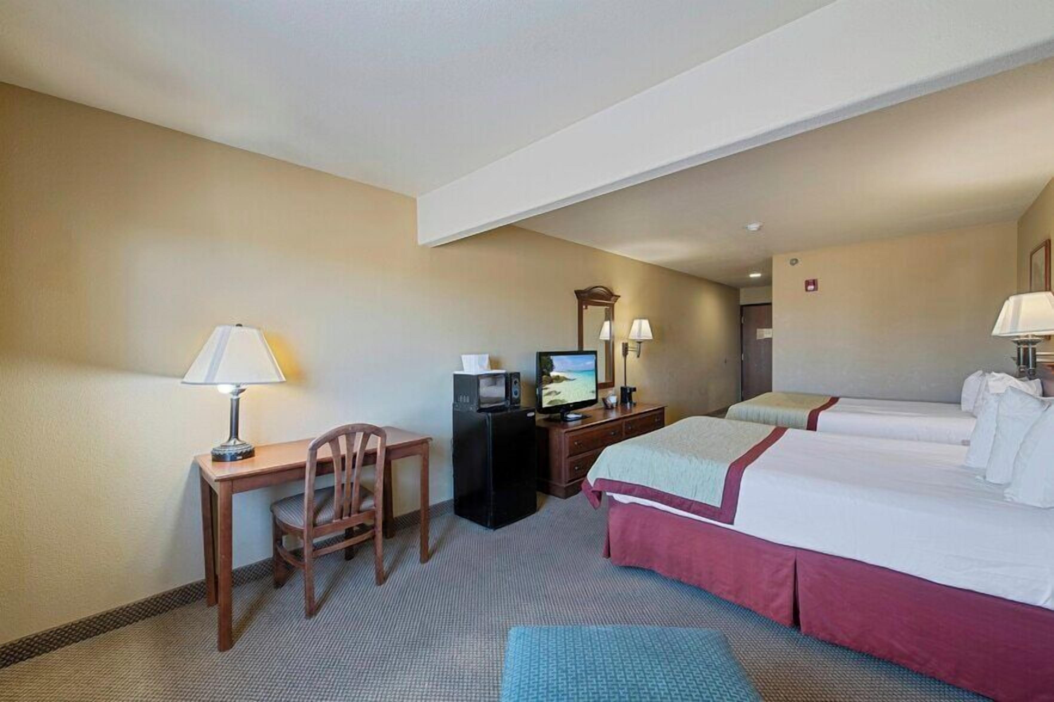 A hotel room with a desk, two beds, a television, and a mirror.