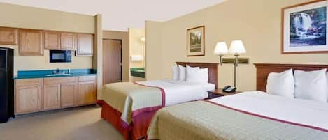 A hotel room with two beds, a kitchenette, a bathroom, and a painting on the wall.