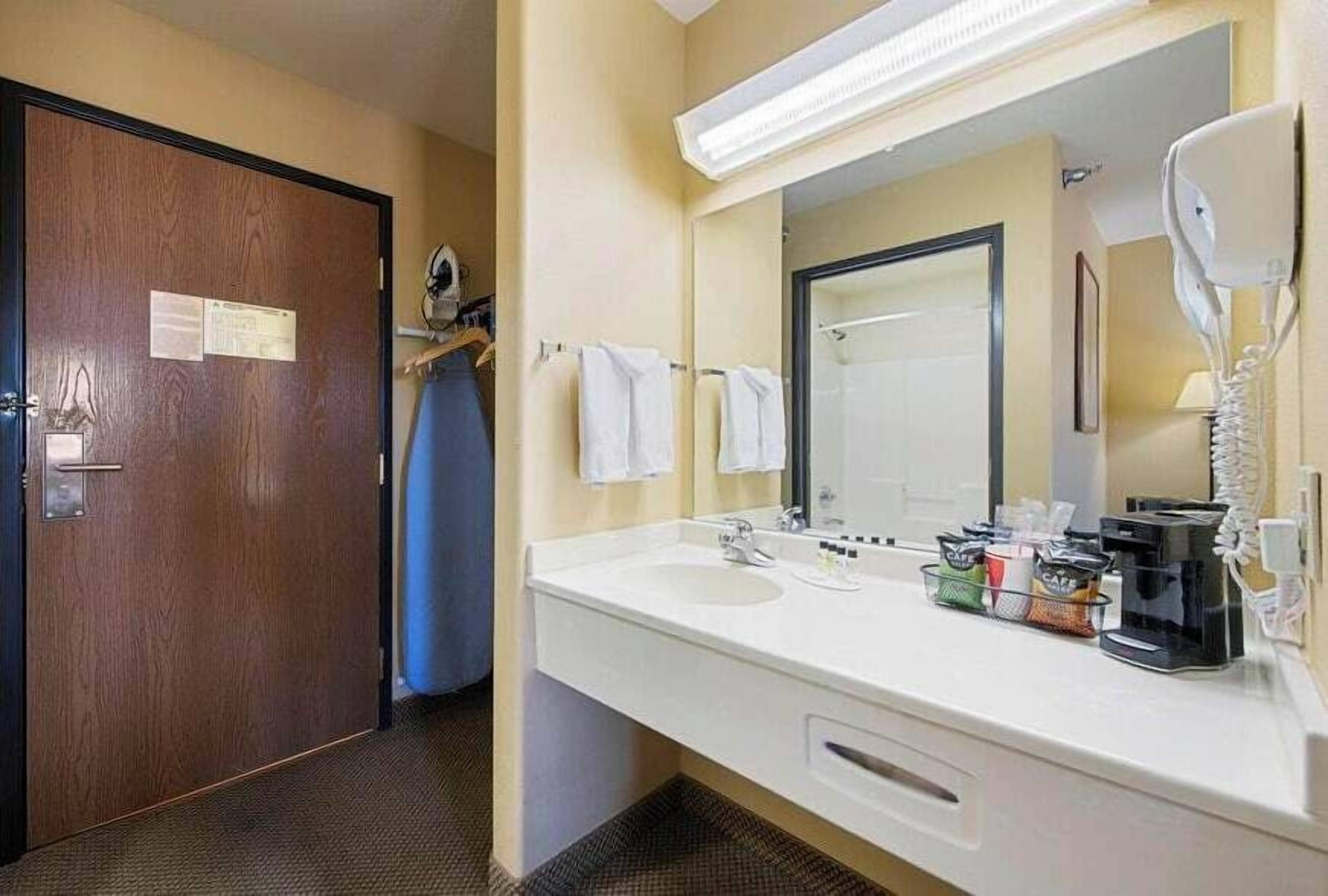 A hotel bathroom with a wooden door, a white sink, a mirror, and a towel rack.