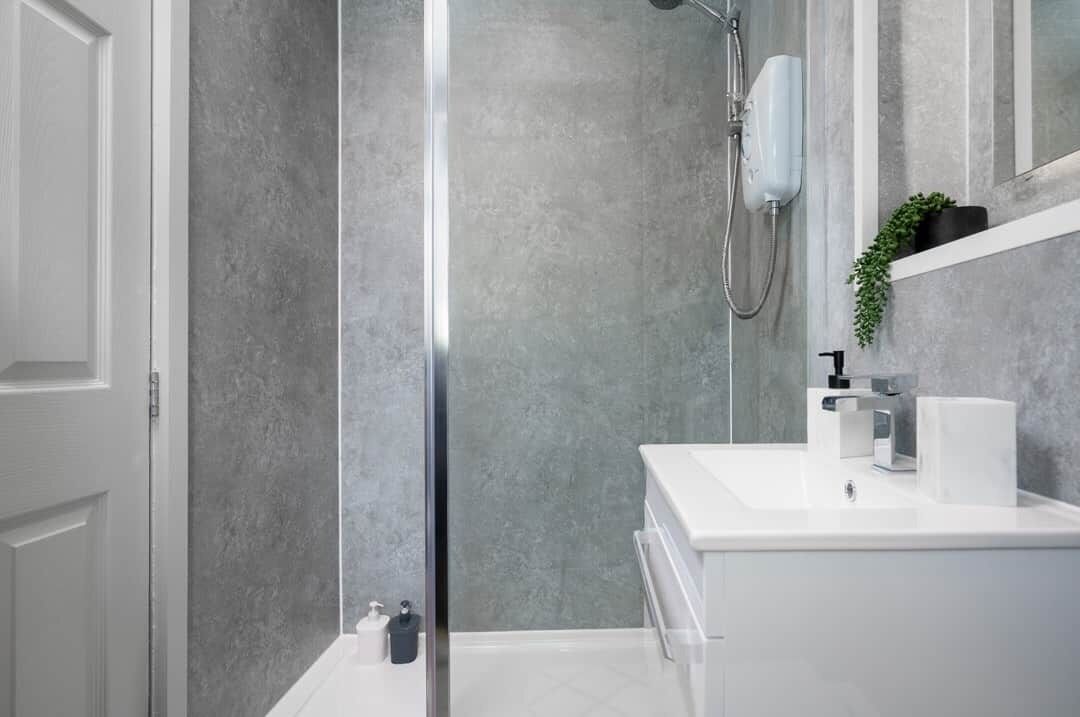 A modern bathroom with a glass shower enclosure, a white sink, and a mirror above it.