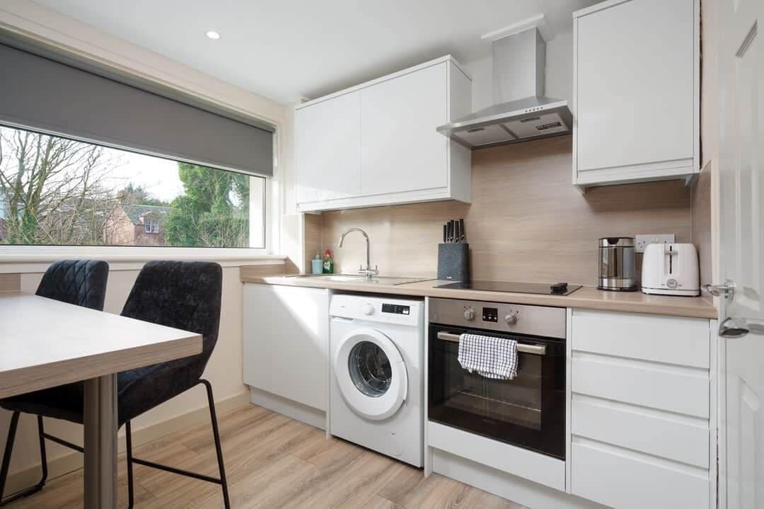 A compact kitchen with a washing machine, oven, and white cabinets.