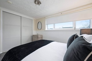 A bedroom with a bed, a window, a mirror, and a wardrobe. - 2BR · Sleeps 6 · Parking · Near Linlithgow Palace (Linlithgow)