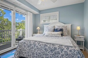 A bedroom with a bed, two bedside tables, a window with blinds, a ceiling fan, and a balcony with a chair. - Bayfront TC Condo · Walk to Beach & Downtown · Free Parking · Sleeps 6 (Traverse City)
