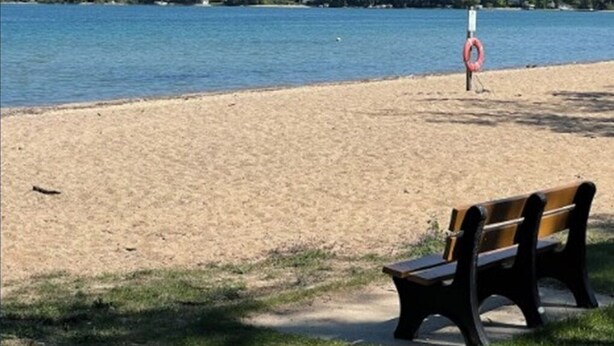 A beach with a bench and a lifebuoy. - Bayfront TC Condo · Walk to Beach & Downtown · Free Parking · Sleeps 6 (Traverse City)