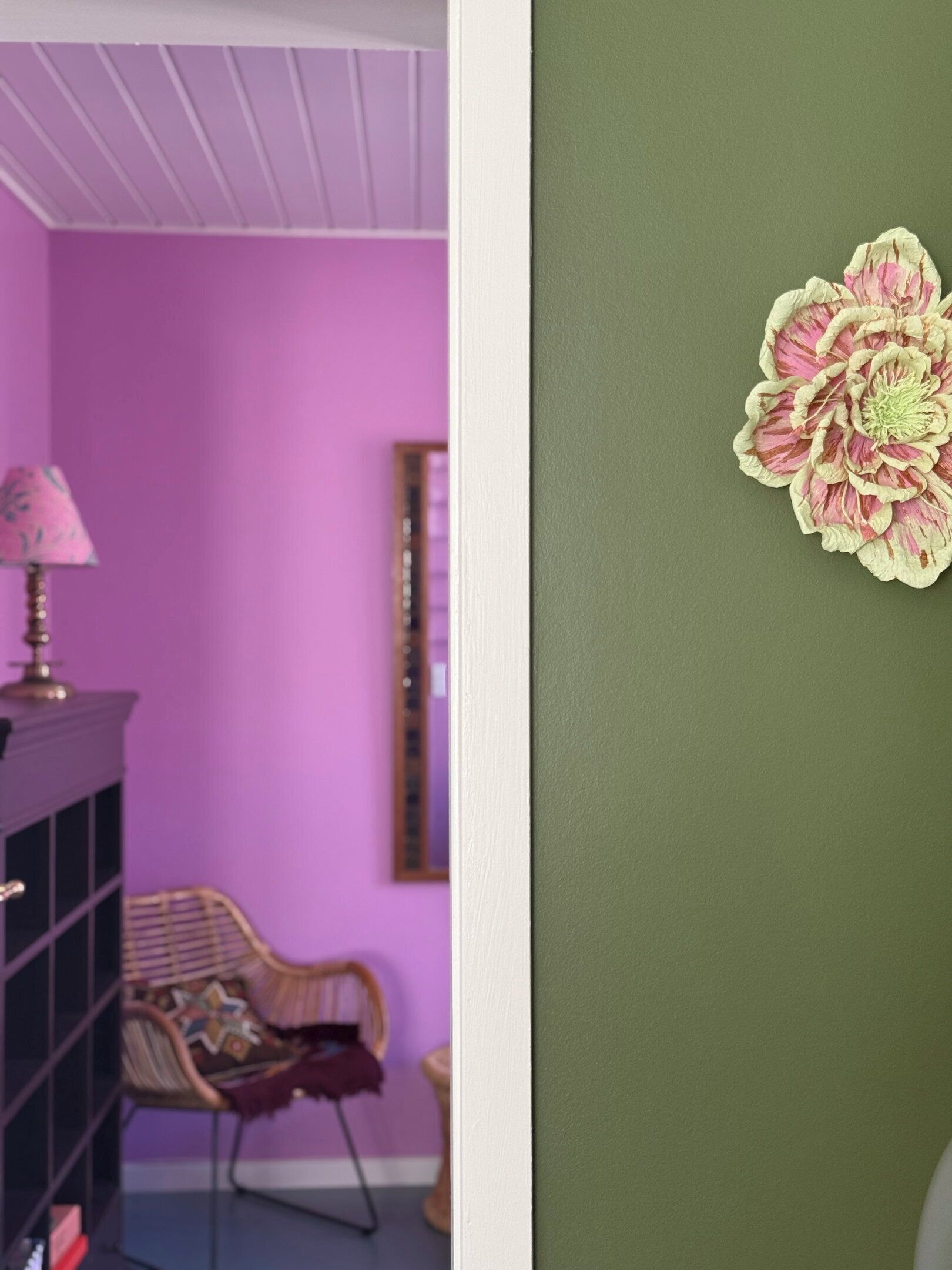 Een kamer met een paarse muur, een houten kast, een stoel en een decoratieve bloem aan de muur.