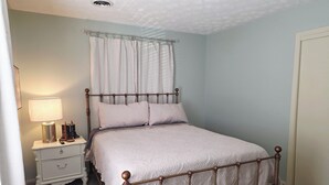 A bedroom with a bed, nightstand, lamp, and curtains.