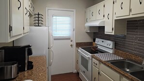 A compact kitchen with white cabinets, a built-in oven, a stove, and a coffee maker.
