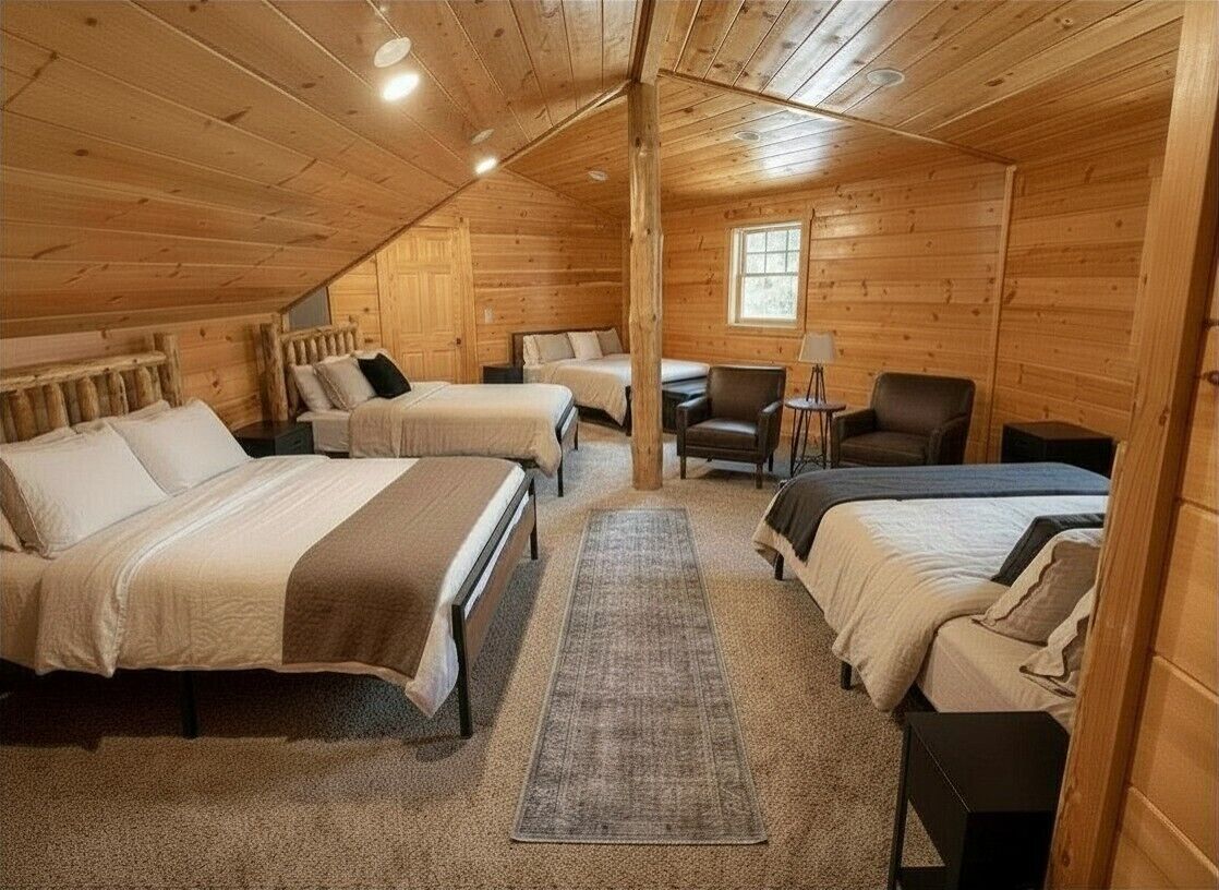 A log cabin bedroom with two beds, a chair, a small table, and a window.