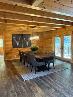 Ein Zimmer mit Holzwänden, einem Esstisch, Stühlen, einer Pendelleuchte und zwei an der Wand befestigten Hirschschädelbildern.