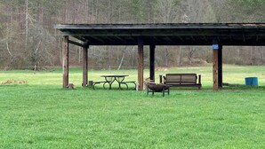 A covered picnic area with a bench, picnic table, and a blue trash bin. - Tempest Ranch Camp is perfect for nature lovers. Close to Watkins Glen. (Beaver Dams)