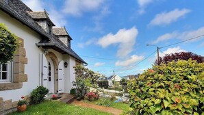 Um edifício de pedra tradicional com fachada branca, telhado em telhas e um jardim bem cuidado com diversas plantas e flores.
