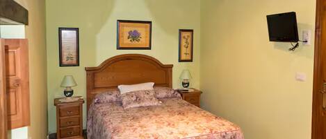 A bedroom with a wooden bed, two bedside tables, a television mounted on the wall, and framed artwork on the walls.