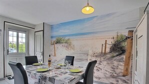 Een eethoek met een strandschildering, een tafel gedekt voor vier personen en een hanglamp.