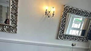 A dining area with a wooden table, chairs with striped cushions, a vase with flowers, and wall-mounted sconces. - Drummond (Limavady)