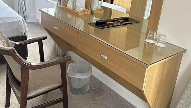 A hotel room with a wooden desk, a chair, a small trash bin, a mirror, and a television mounted on the wall. - Drummond (Limavady)