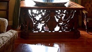 A room with a table featuring a decorative vase, a chair, and a window with curtains. - Drummond (Limavady)