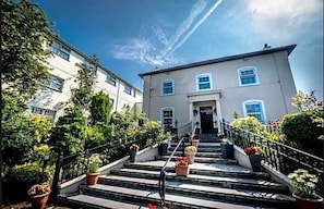 A building with a staircase leading to a door, surrounded by potted plants and a clear sky. - Drummond (Limavady)
