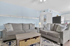 Ein Wohnzimmer mit zwei grauen Sofas, einem kleinen Holztisch und einem Teppich mit Anker-Motiven.