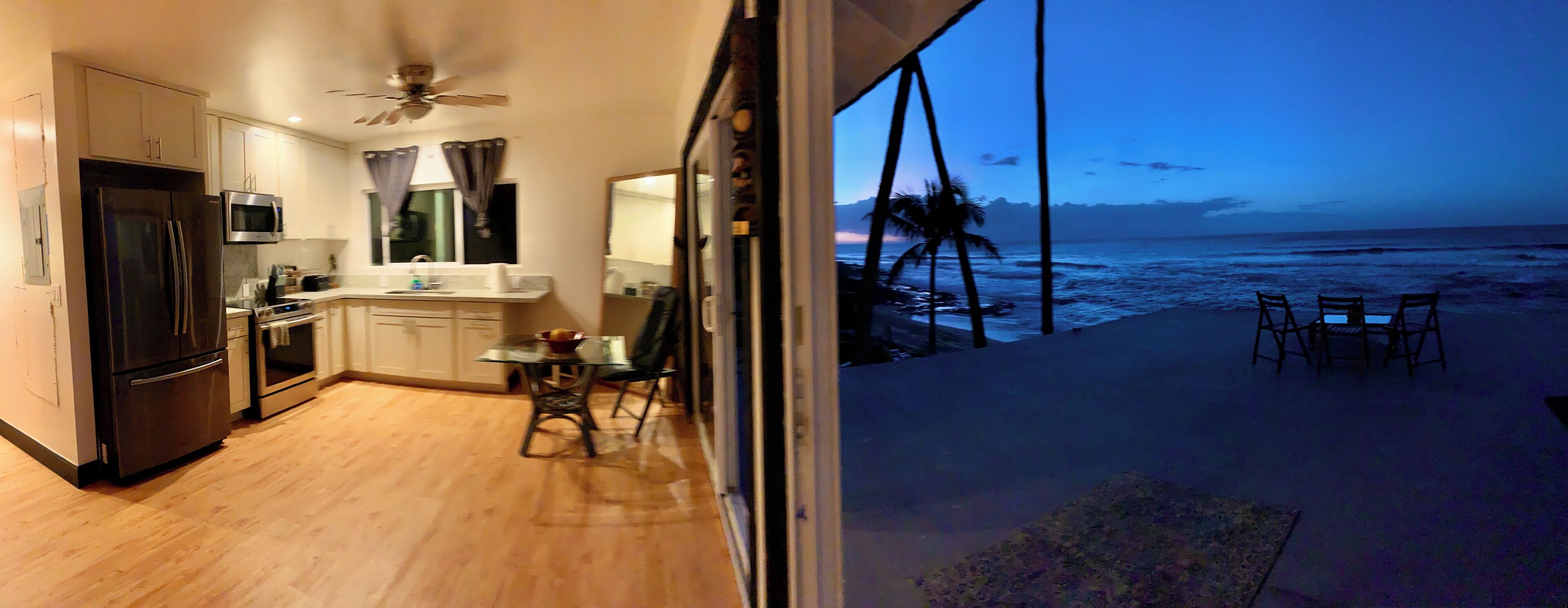 A kitchen with a refrigerator, microwave, and dining area with a view of the ocean.