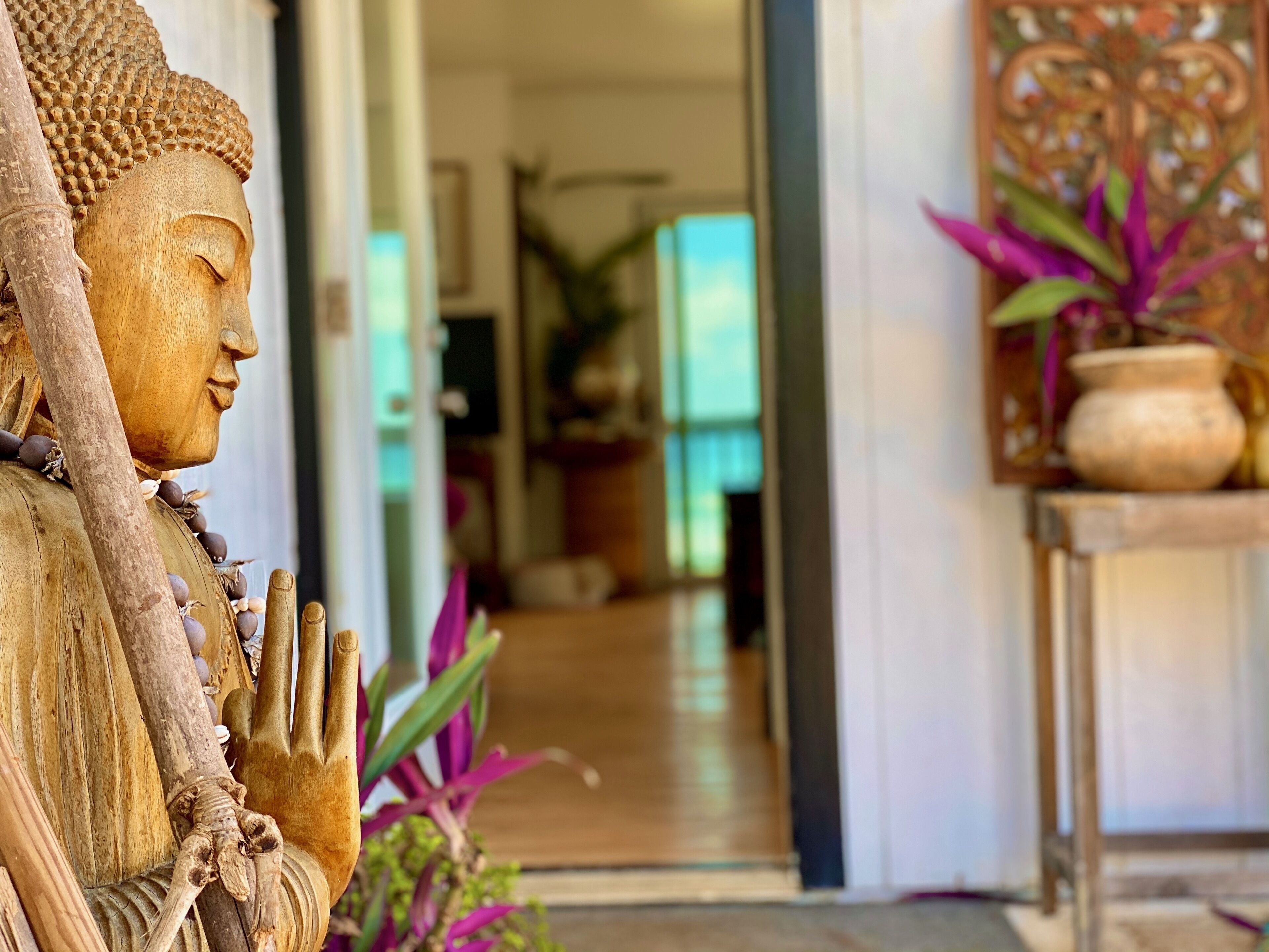 A statue with a serene expression, a wooden structure with a textured surface, and a potted plant with broad leaves.